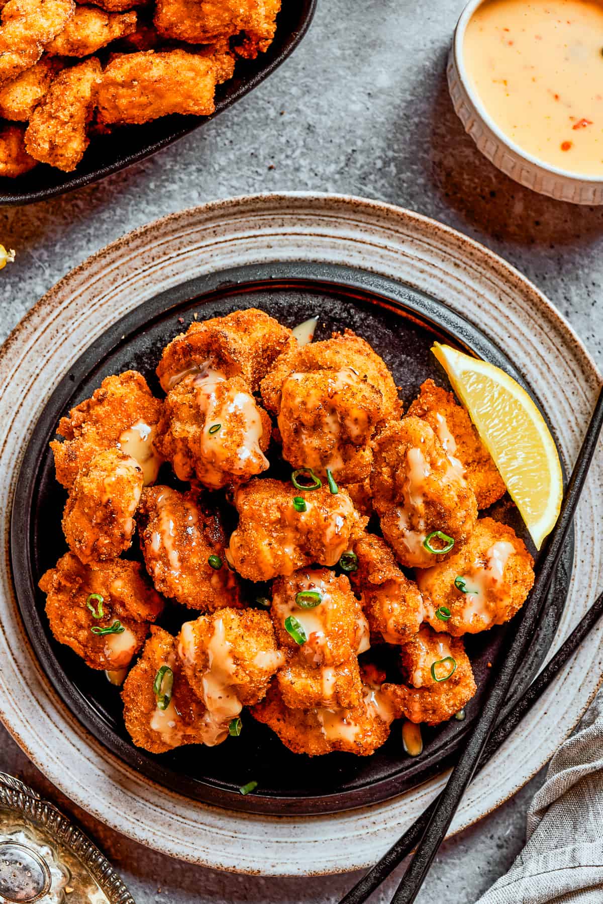 Overhead image of crispy fried bang bang chicken served on a dark dinner plate.