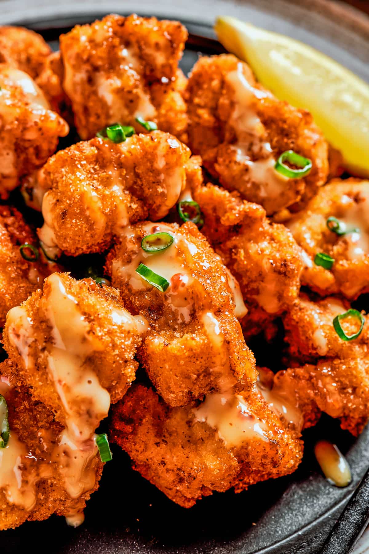 Close-up image of bang bang chicken drizzled with chili mayo sauce and green onions on top.