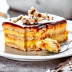 A slice of chocolate eclair cake on a plate, with a fork on the plate with a bite of cake.