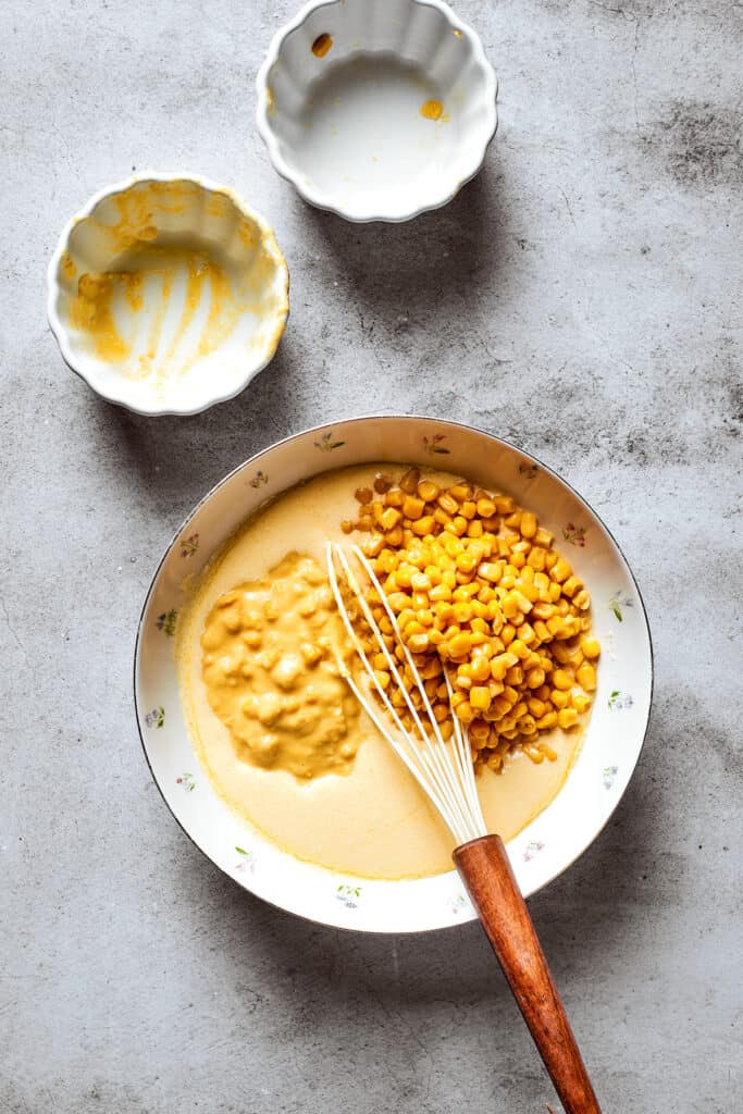 Corn and creamed corn are added to a bowl of souffle base with a whisk.