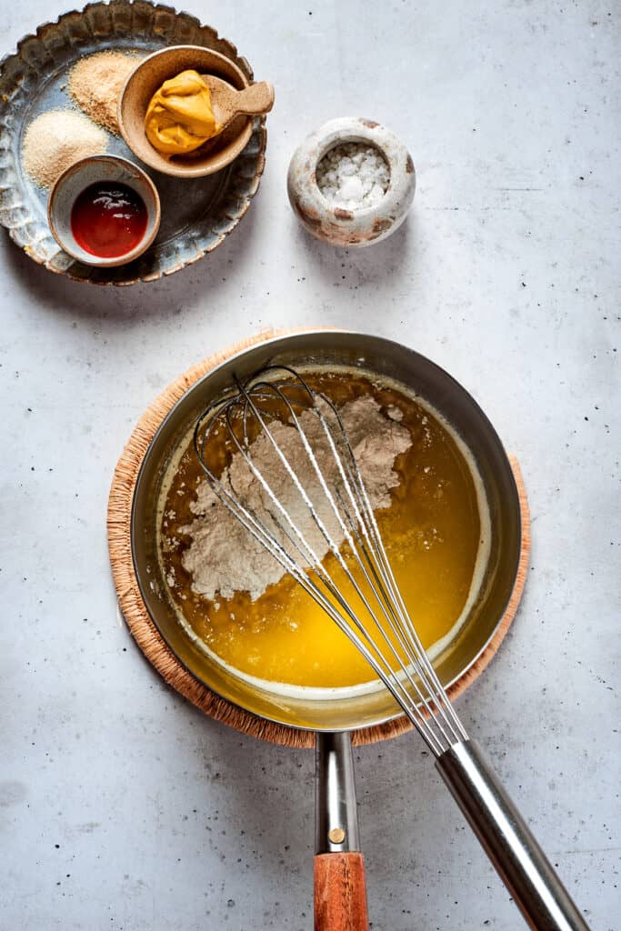A whisk whisks a cheese sauce in a metal pot.