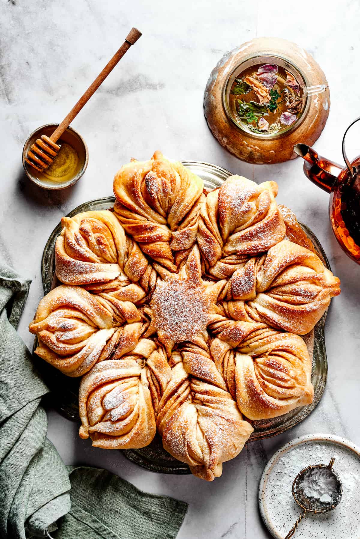 Overhead view of a star bread topped with powdered sugar, next to a bowl of honey.