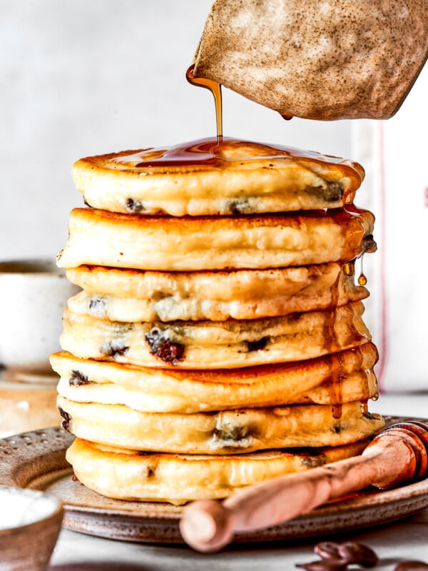 Pouring maple syrup over a stack of chocolate chip pancakes.