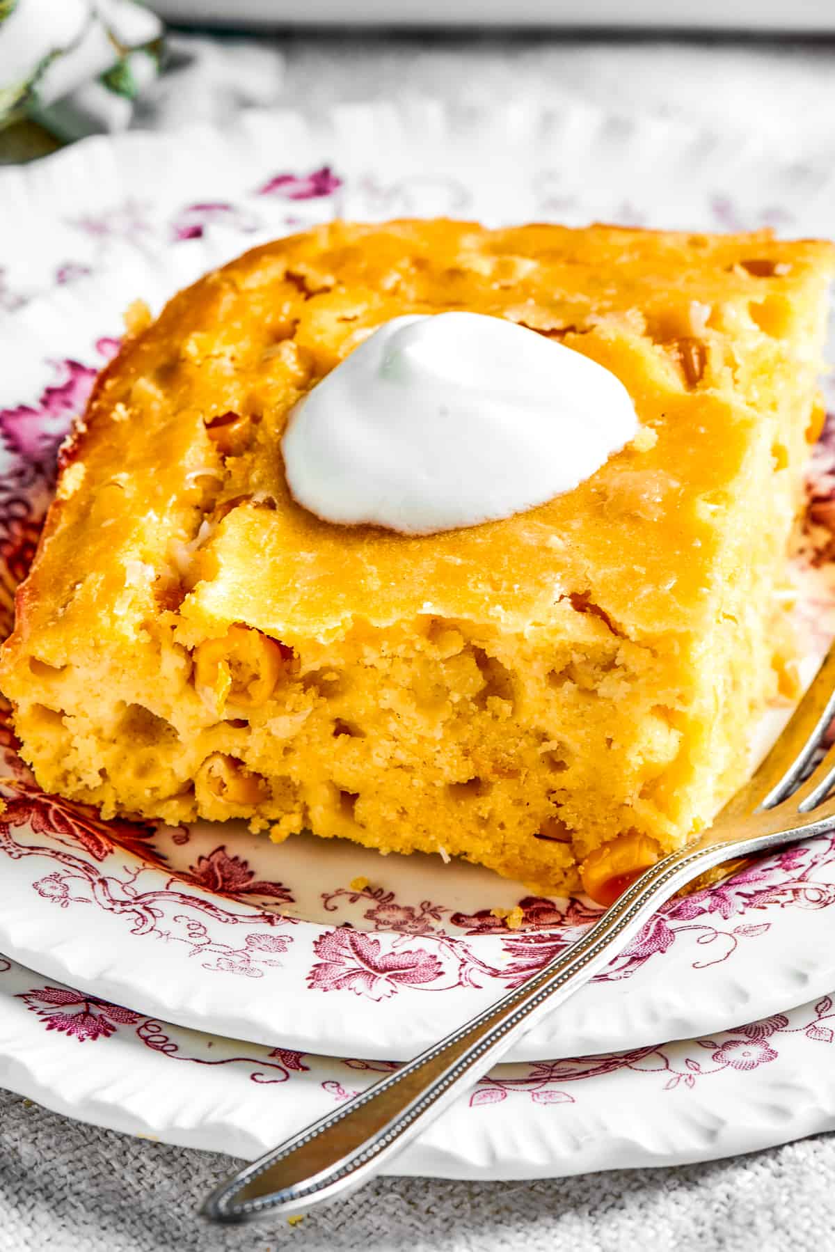 Square of corn souffle served on a dish and garnished with a dollop of sour cream.