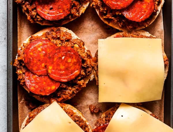 Cheese slices are placed on top of pizza burgers on a tray.