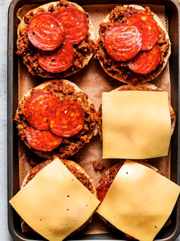 Cheese slices are placed on top of pizza burgers on a tray.