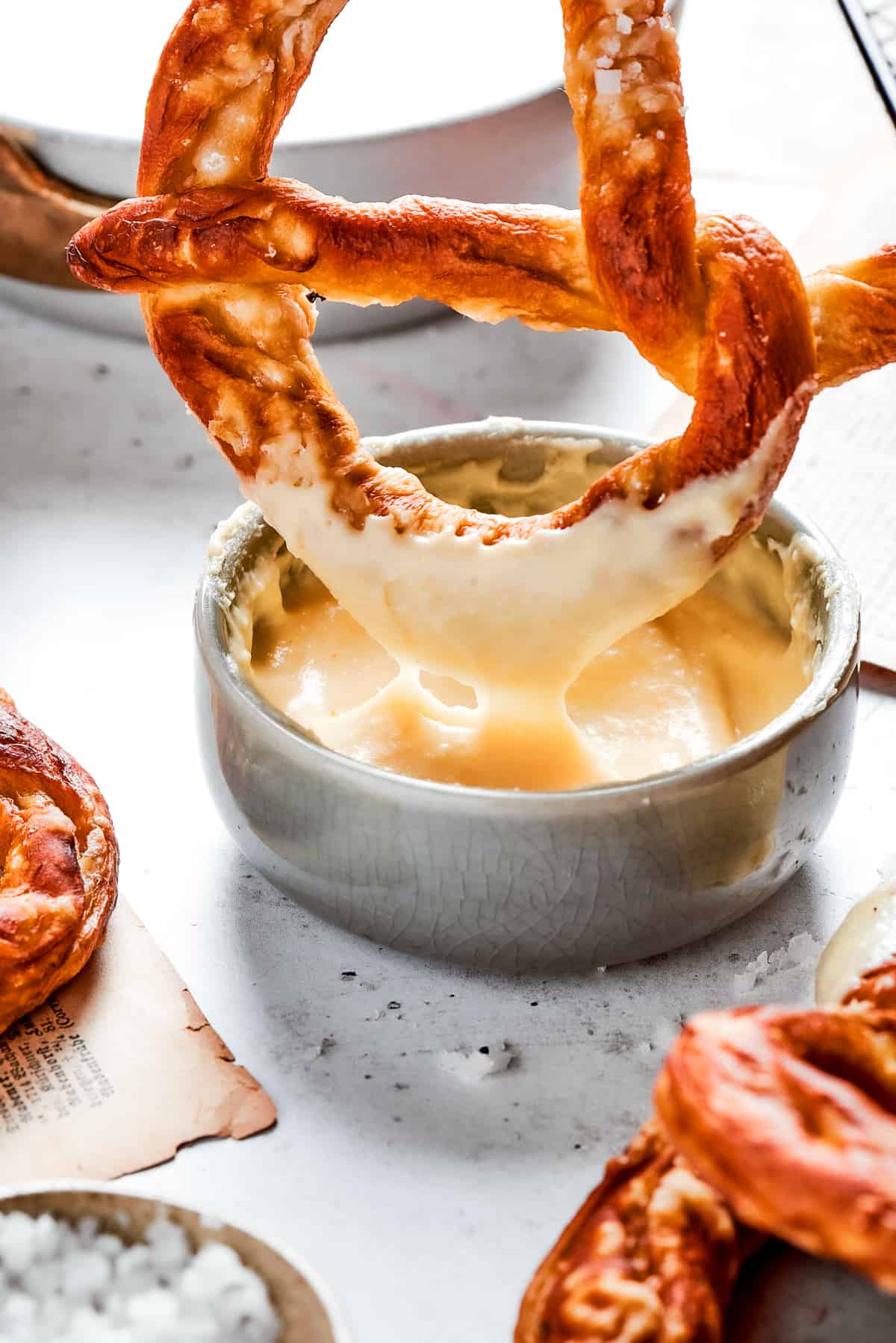 A soft pretzel is dipped in cheese sauce.