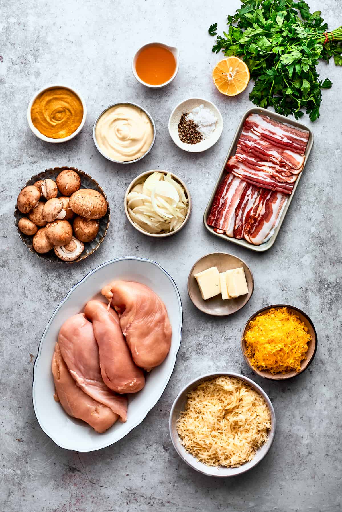 The ingredients to make Alice Springs chicken are shown portioned out: chicken, mushrooms, honey, mayo, mustard, garlic, onion, butter, bacon, salt and pepper, cheddar and Jack cheeses.