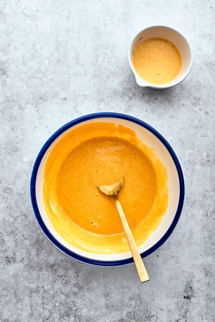 A wooden spoon combines a bright honey mustard marinade in a bowl.