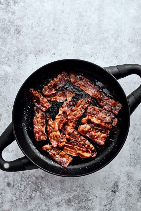 Browning bacon slices in a cast iron pot.