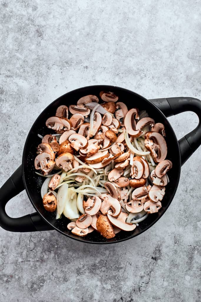 Garlic, onion, and sliced mushrooms are added to a cast iron pot.