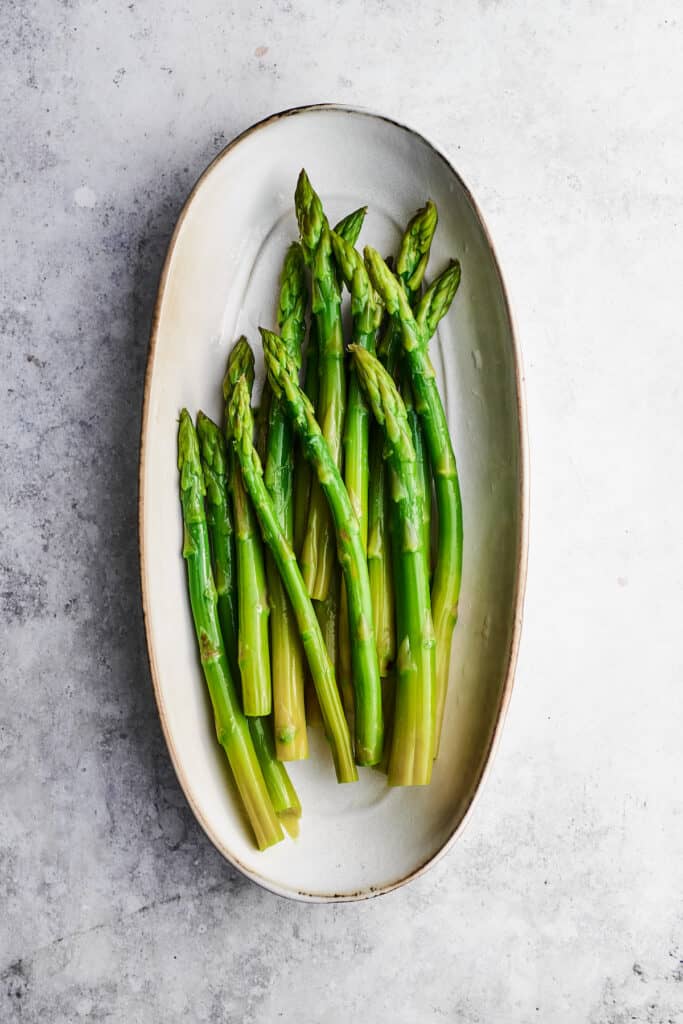 Asparagus for chicken madeira are arranged in an oval white baking dish.