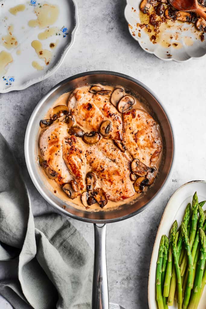 A metal skillet of chicken madeira with cooked chicken, mushrooms, and a cream sauce.