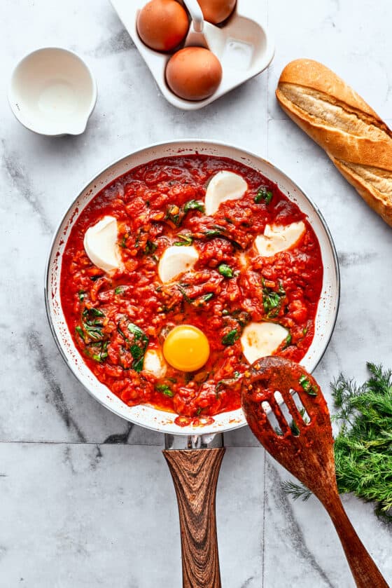 Eggs are added to a skillet of tomato sauce, spinach, and cheese.