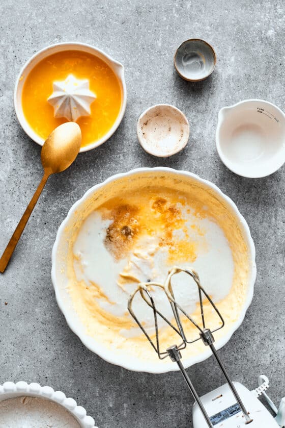 Vanilla paste and orange juice are mixed into a bowl of orange cake batter.