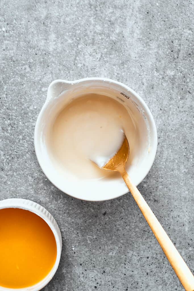 A white bowl of orange glaze is mixed with a wooden spoon.