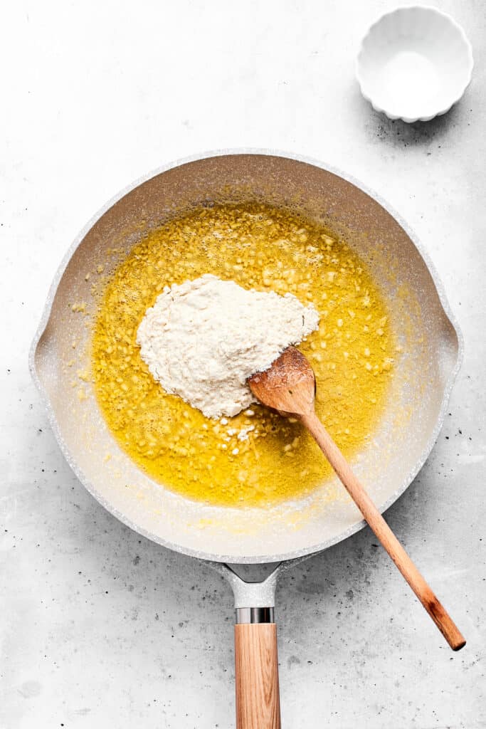 Adding flour to hot garlic butter in a saute pan.