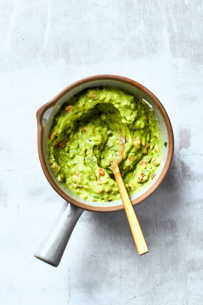 A wooden spoon stirs a bowl of guacamole.
