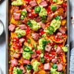 A baked pan of steak nachos is topped with dollops of guacamole and chunks of steak.