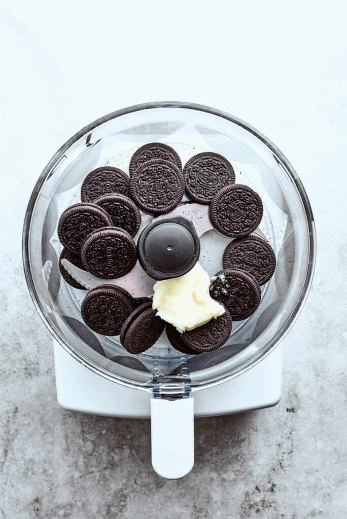 Chocolate cookies are placed in a food processor with a pat of butter.