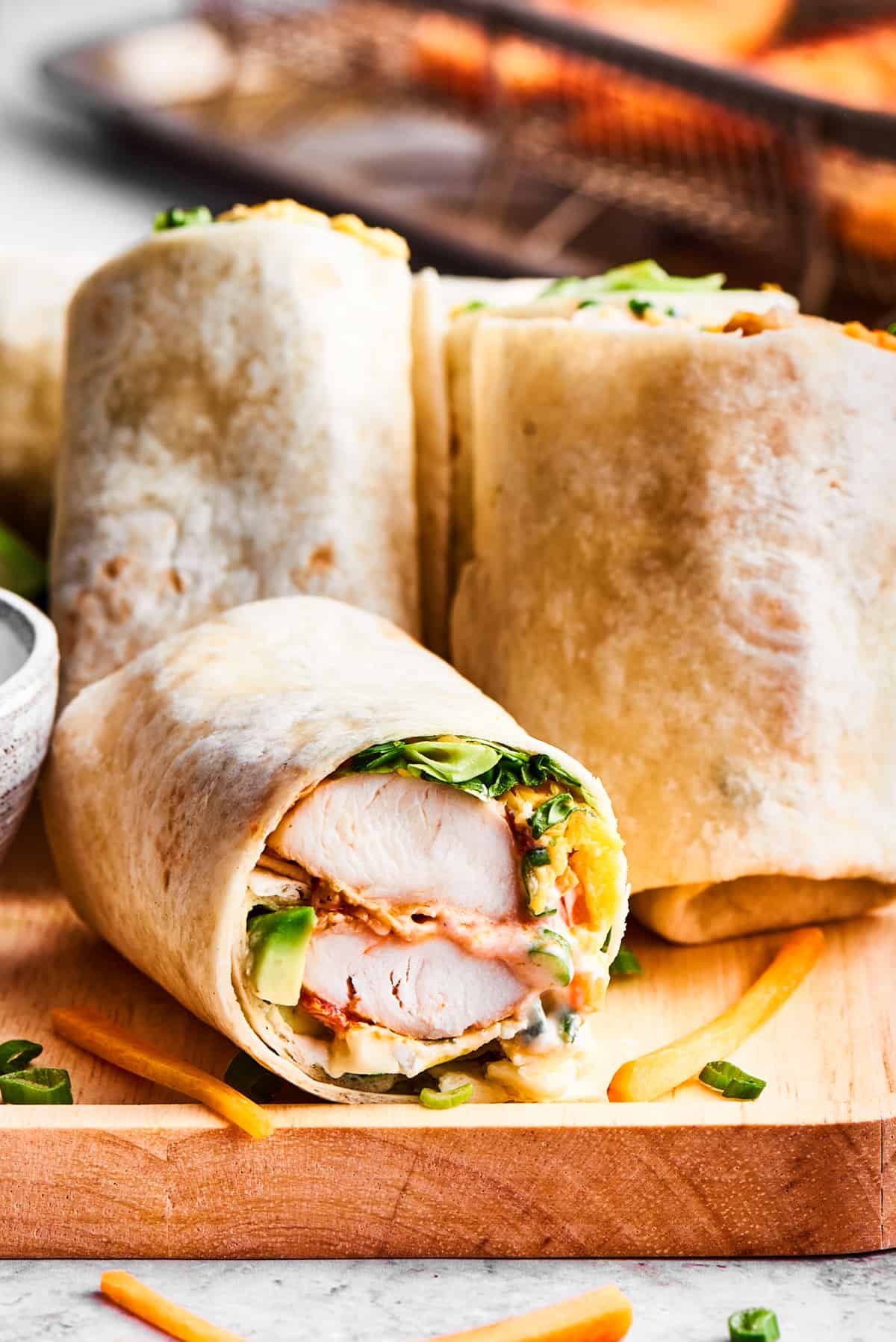 Sliced buffalo chicken wraps are displayed on a wooden cutting board with a bowl of ranch dressing nearby.
