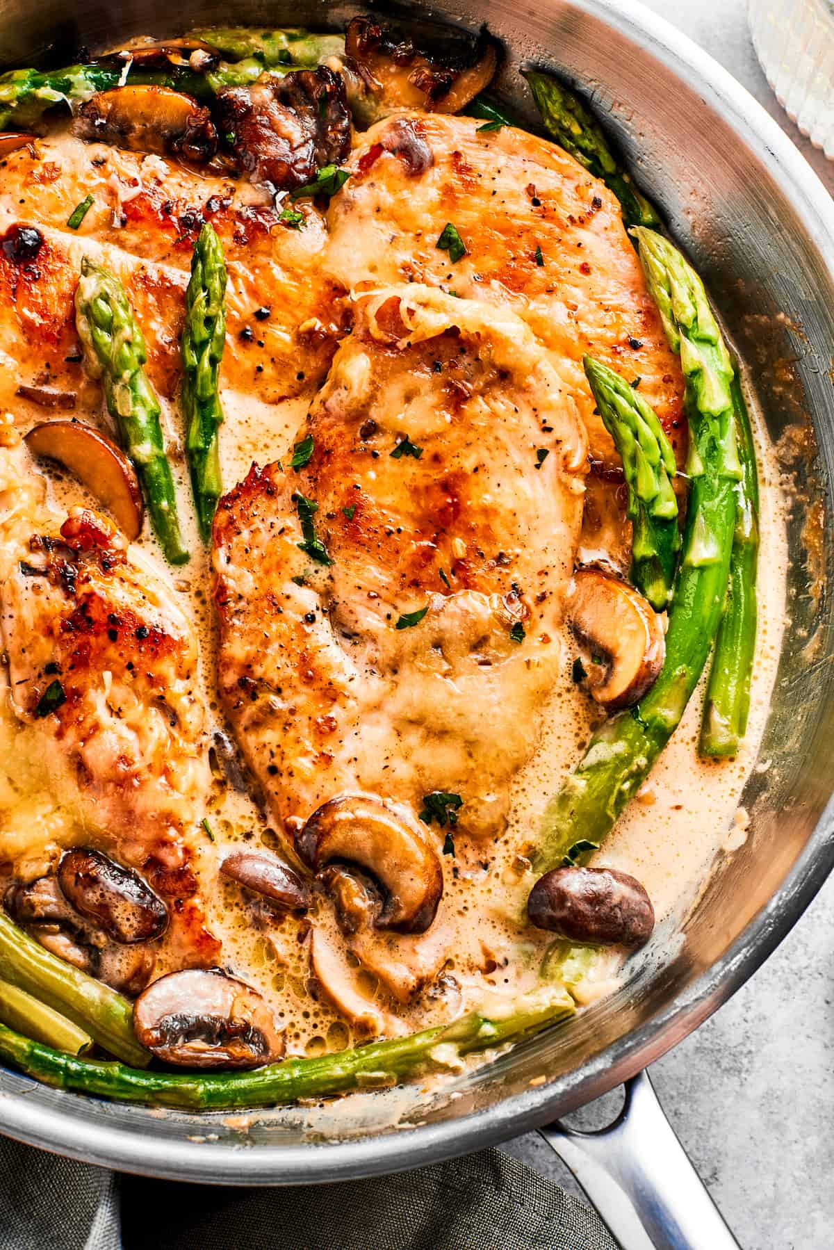 Close-up photo of chicken Madeira and asparagus spears cooking in a skillet.