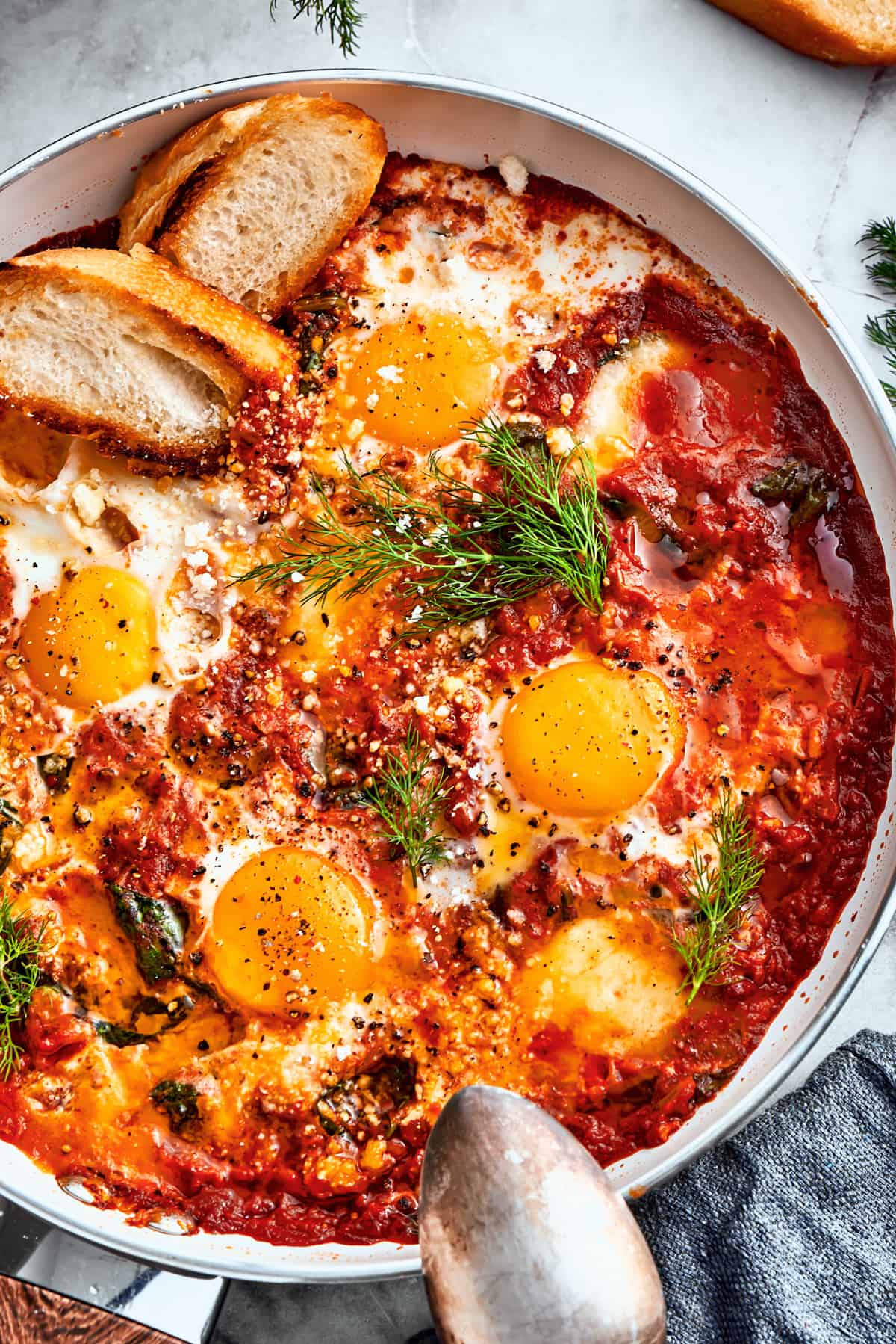 Overhead up close image of a skillet with cooked eggs in purgatory and garnished with parsley and toasted bread.