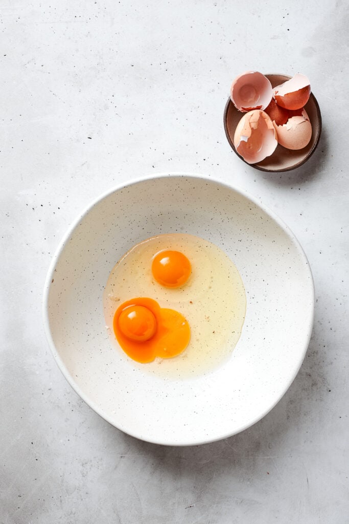 Two eggs and an egg yolk in a white bowl.