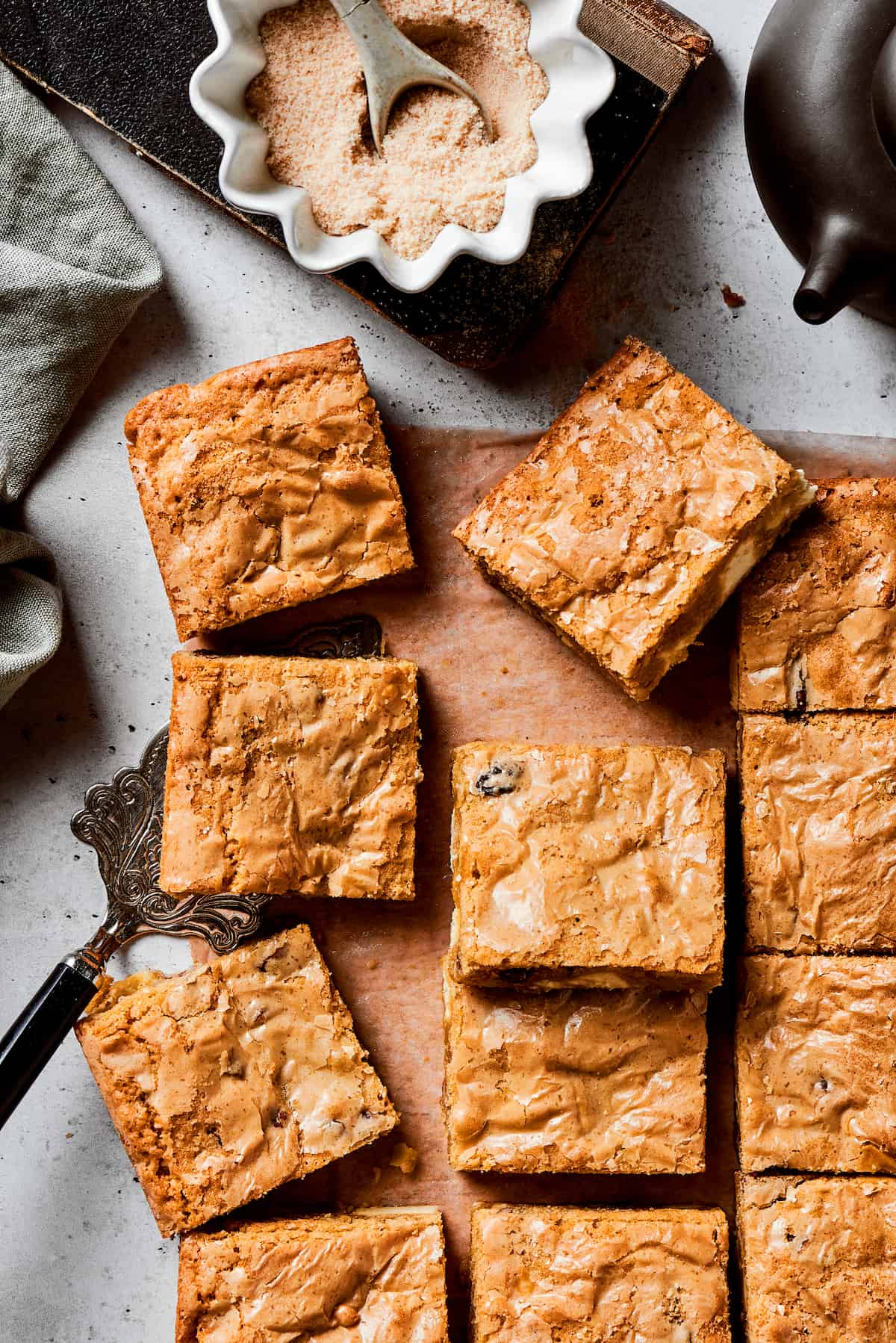A cutting board of blonde brownie squares with a bowl of brown sugar next to it.