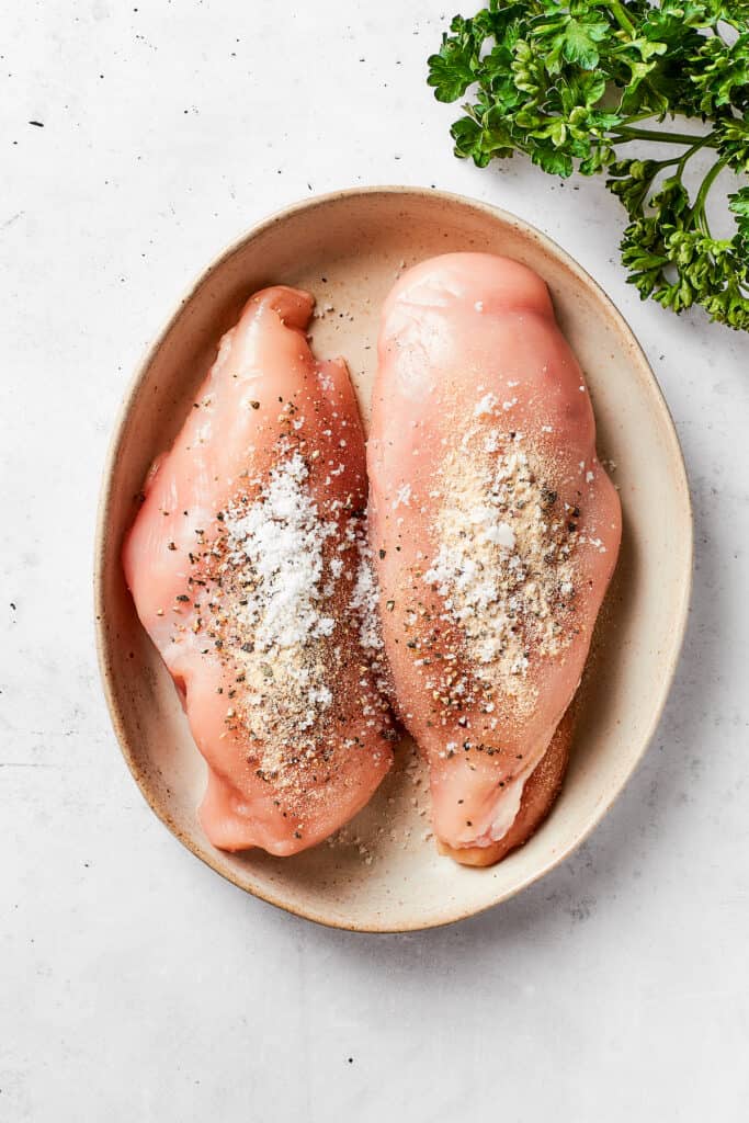 Two seasoned chicken breasts rest in an oval serving dish.