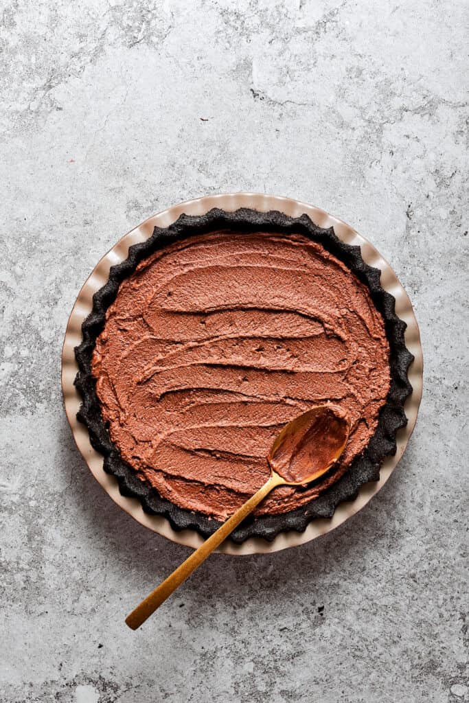 A spoon smooths french silk pie filling into a pie crust.