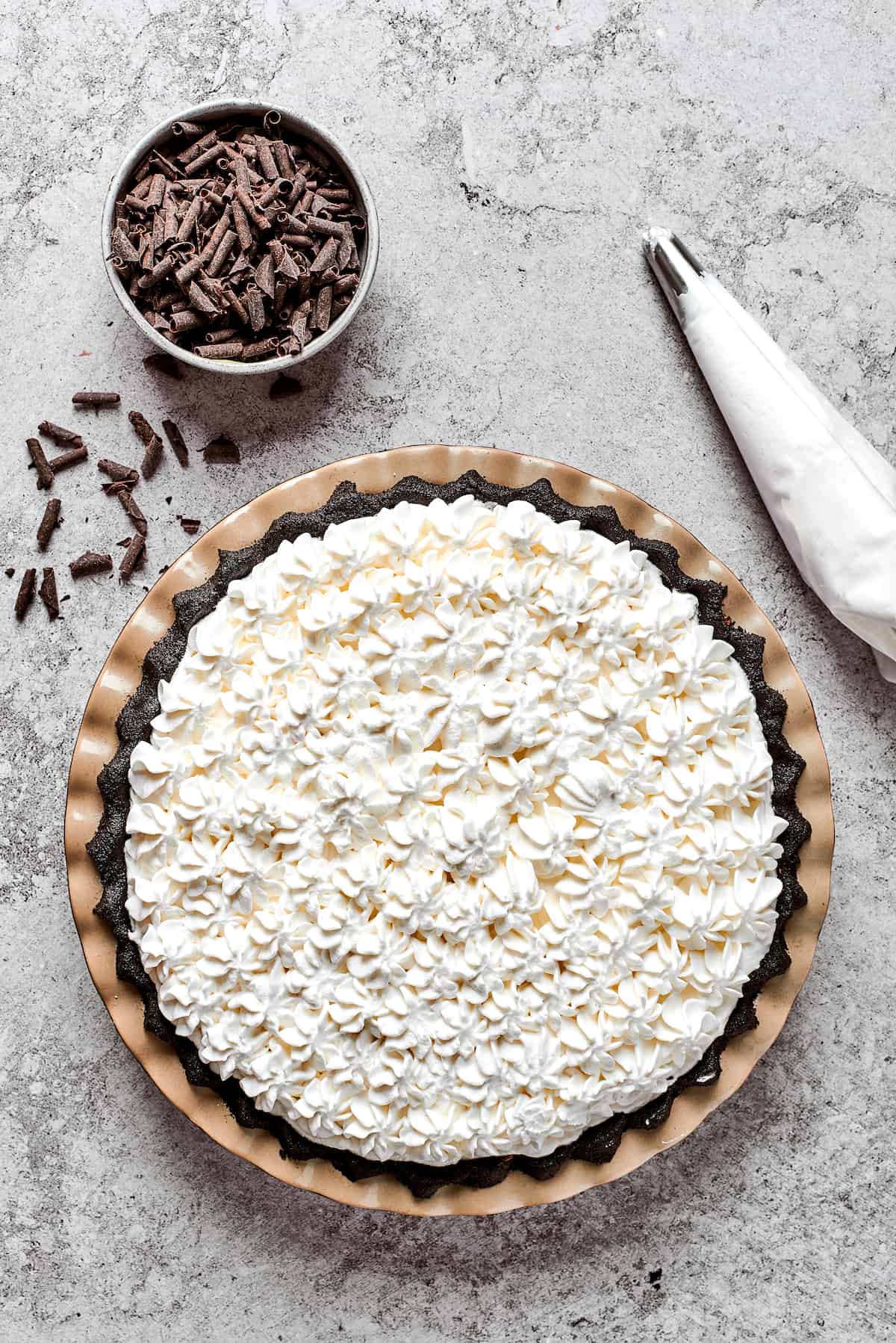 Whipped cream is piped on top of a French silk pie.