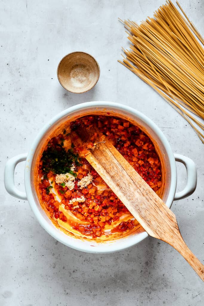 A wooden spoon stirs ingredients into a pot of spicy chicken soup.