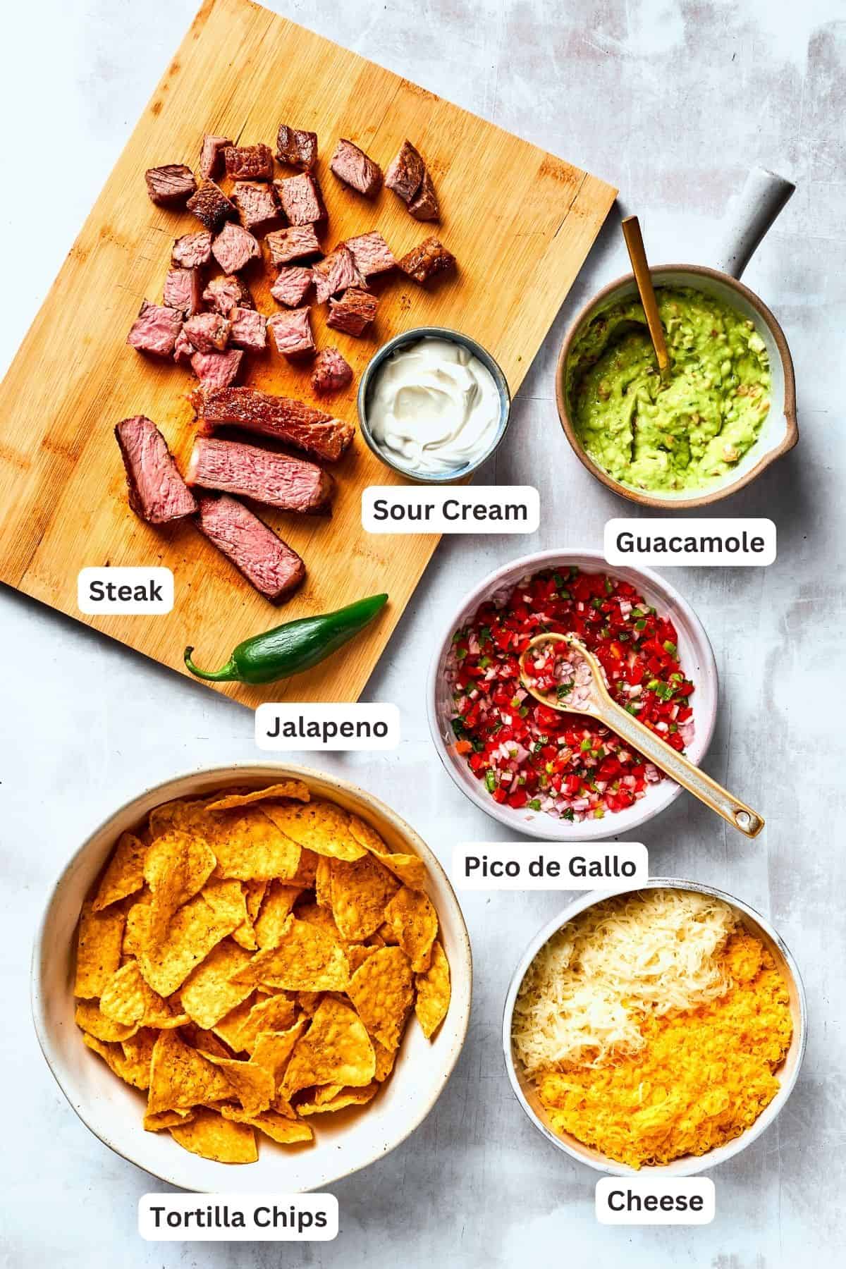 Ingredients for steak nachos are shown portioned out - guacamole, steak, pico de gallo, chips, and cheese.
