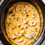 Overhead image of Shredded chicken in a creamy sauce cooking in a black slow cooker.