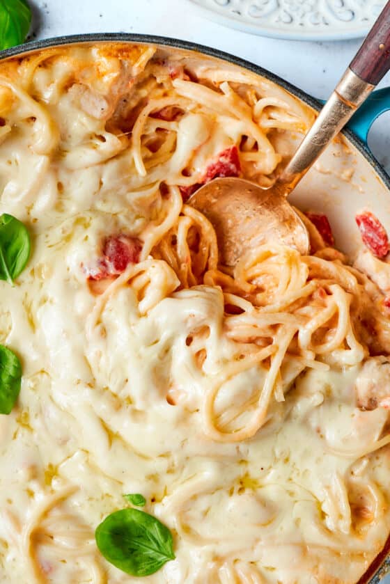 A spoon digs into a pot of cheesy chicken spaghetti.