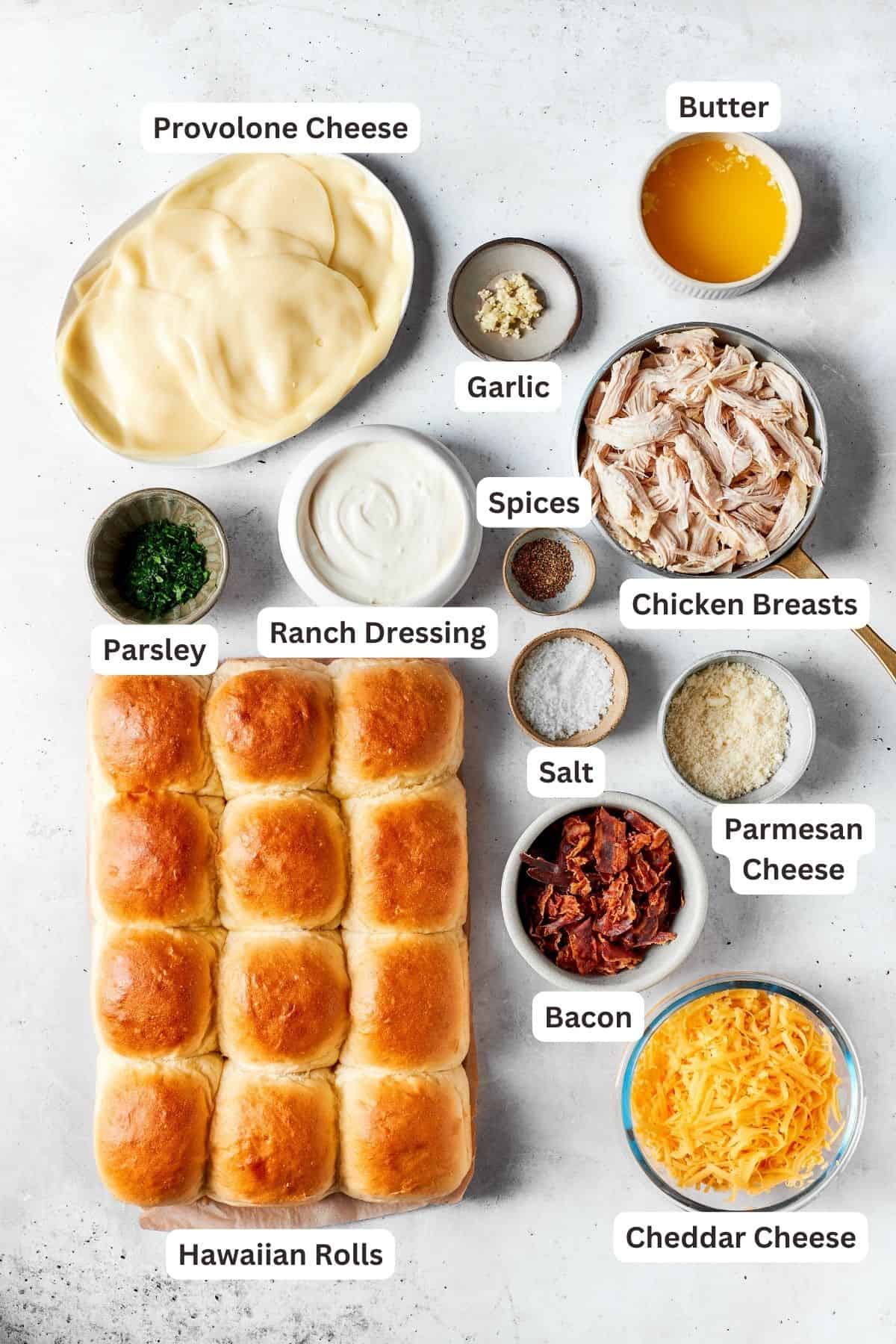 The ingredients for chicken bacon ranch sliders are shown: sweet rolls, provolone cheese, cheddar cheese, parmesan cheese, shredded chicken, salt, bacon, ranch dressing, parsley, garlic, spices.