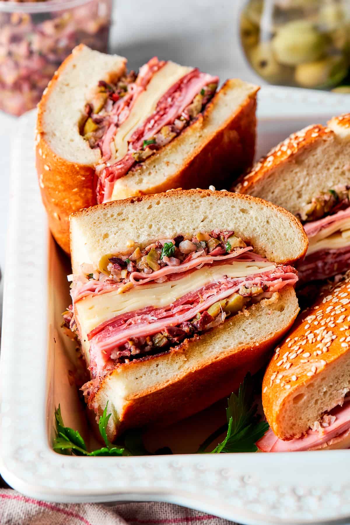 Pieces of muffaletta sandwich are shown on their sides with meat and cheese visible.