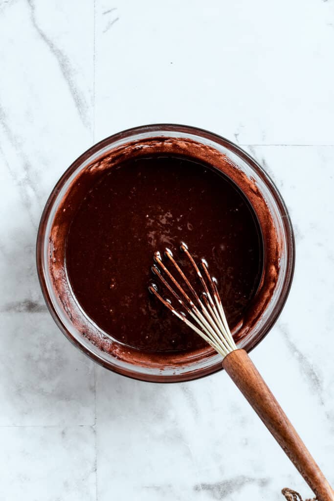 A whisk blends a bowl of brownie batter.