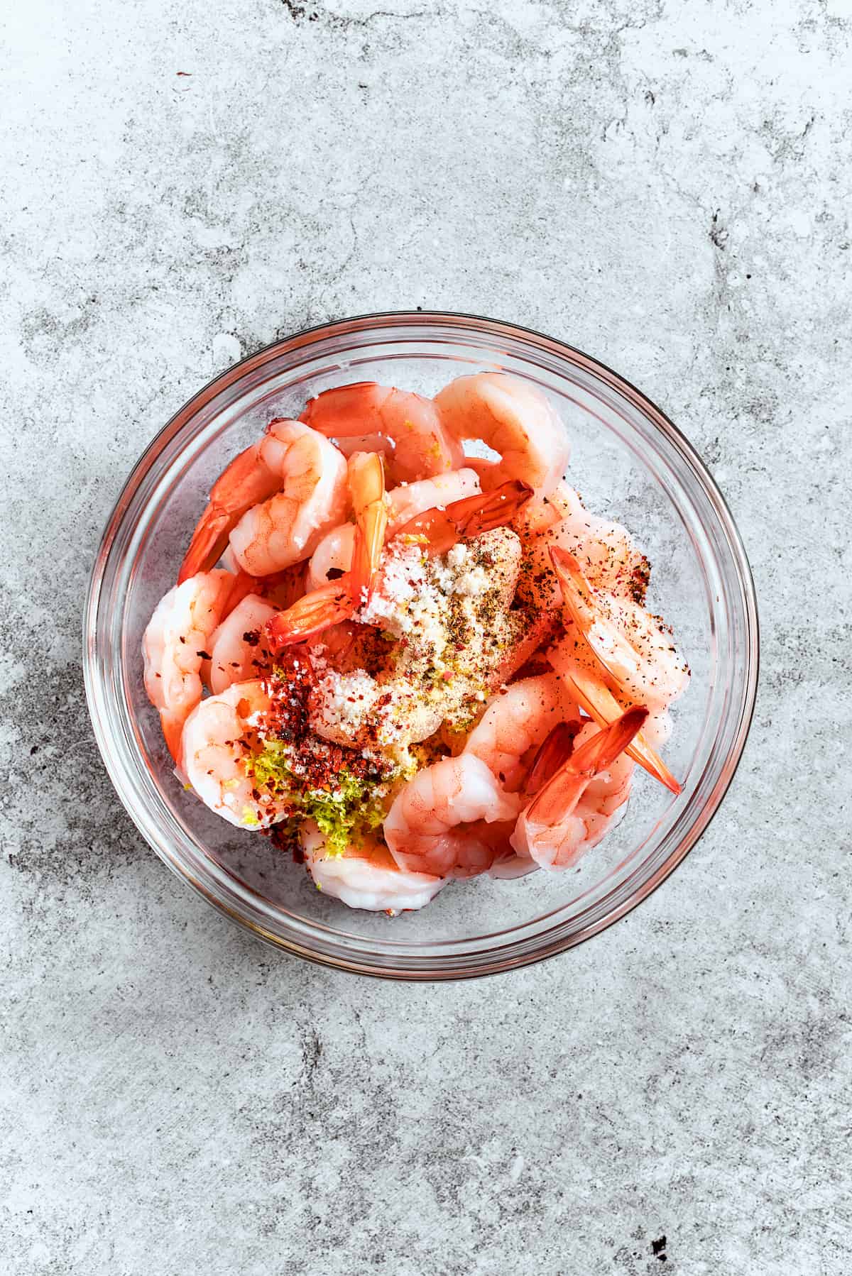 Seasoning the shrimp for maximum flavor. Raw shrimp being tossed with a blend of vibrant seasonings in a mixing bowl, preparing them for cooking.