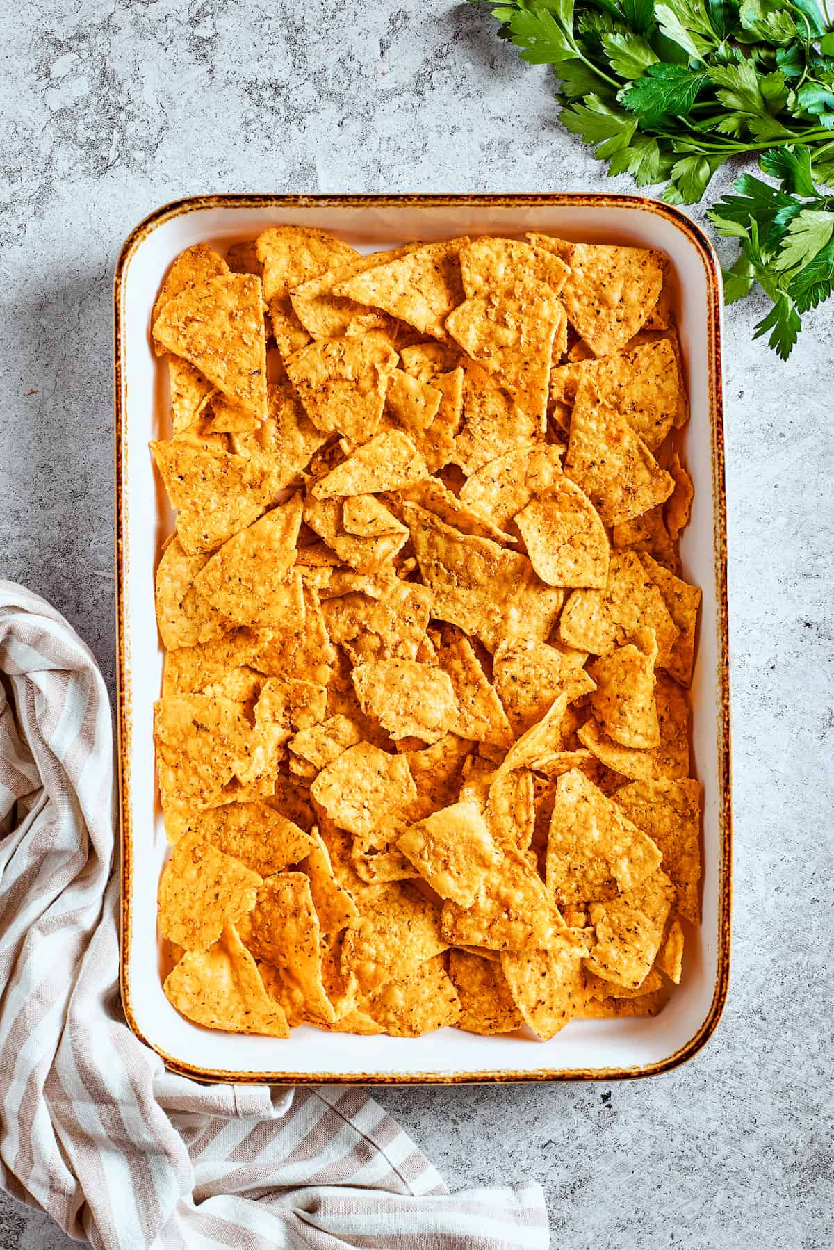 The base layer of crispy tortilla chips. Tortilla chips neatly arranged in a single layer on a baking tray, ready for toppings.