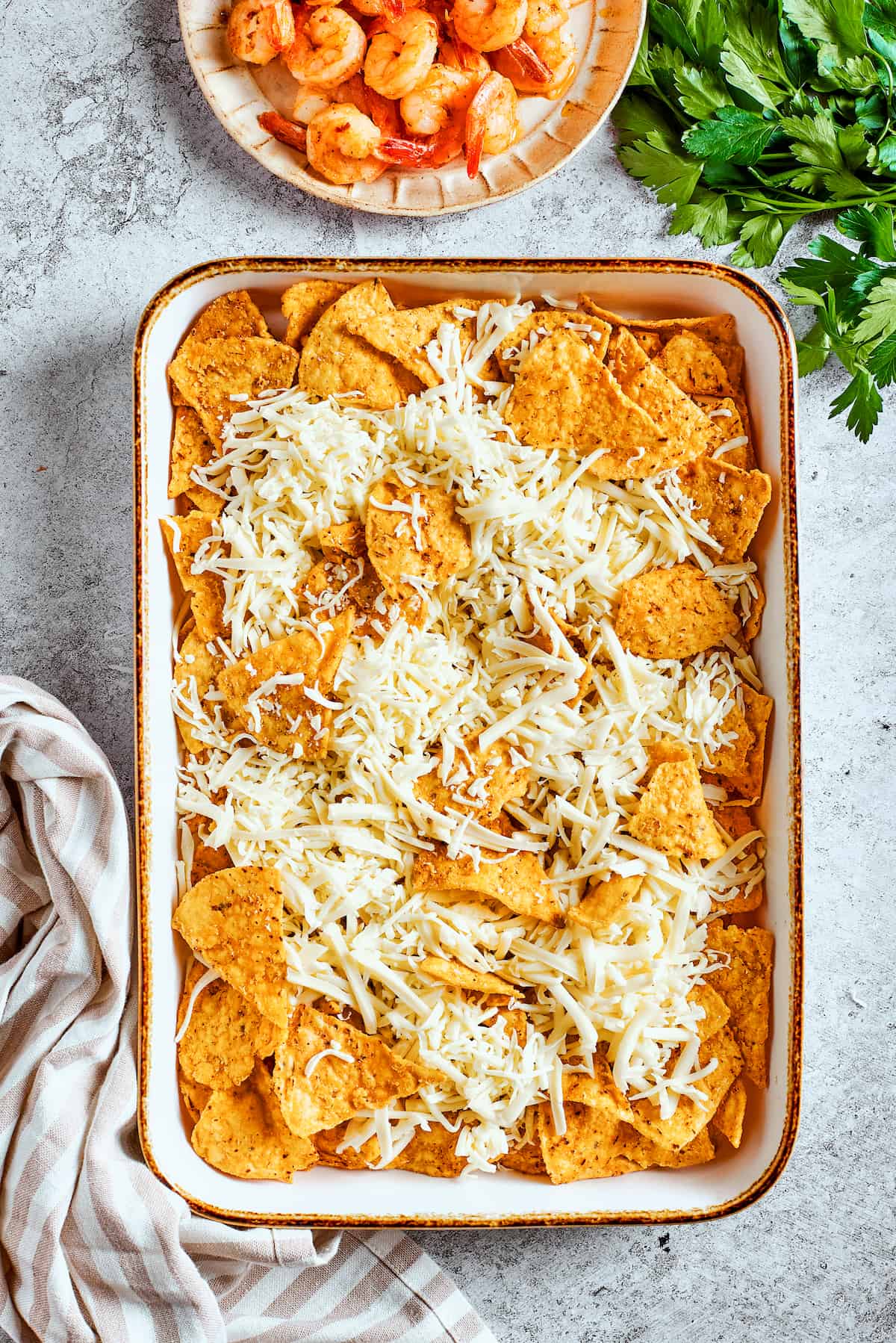 Adding the essential layer of cheese. A generous sprinkling of shredded cheese being added over the arranged tortilla chips on a baking tray.