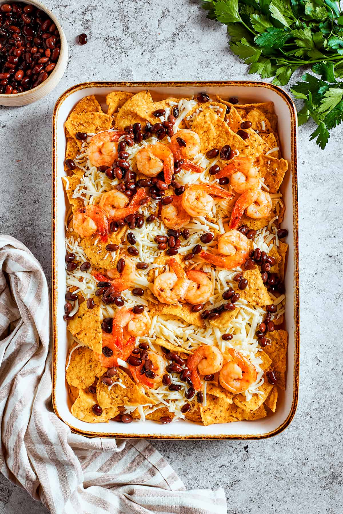 Layering the delicious toppings. Cooked shrimp and black beans scattered over the cheesy tortilla chips on a baking tray, ready for the oven.