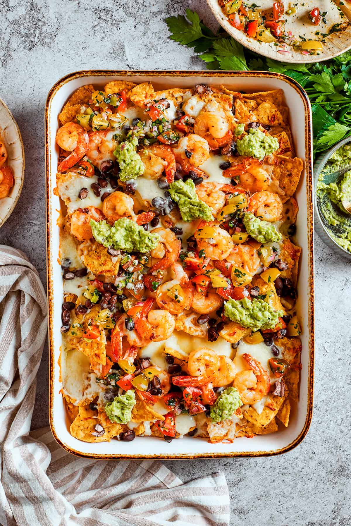 The finishing touch: fresh guacamole. Creamy homemade guacamole being dolloped artfully onto the freshly baked and garnished tray of shrimp nachos.