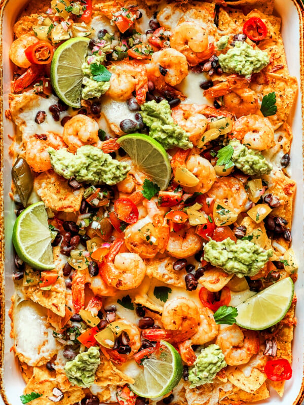 Nacho chips topped with shrimp, cheese, black beans, tomatoes, and a garnish of guacamole and slices of lime.