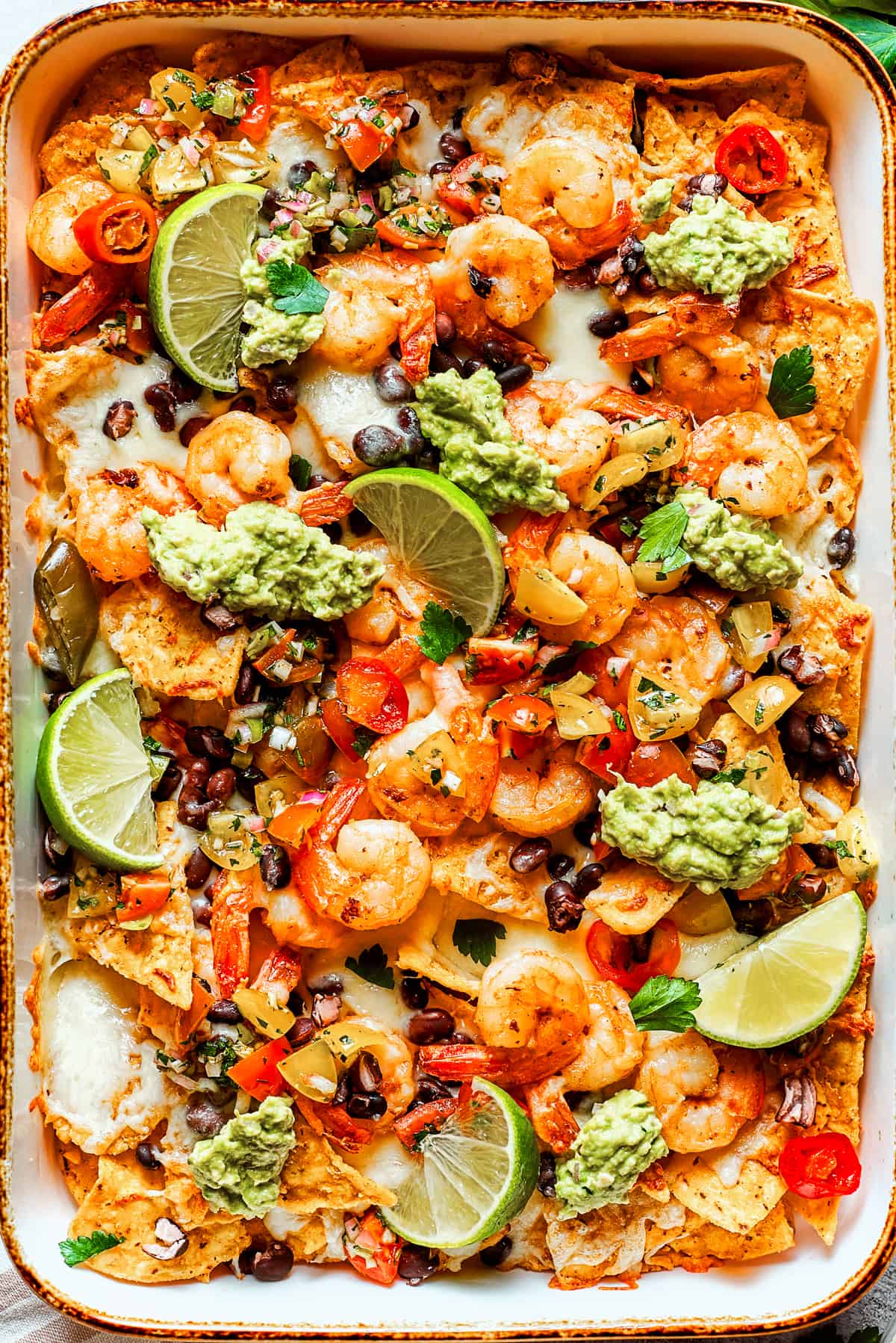 Nacho chips topped with shrimp, cheese, black beans, tomatoes, and a garnish of guacamole and slices of lime.
