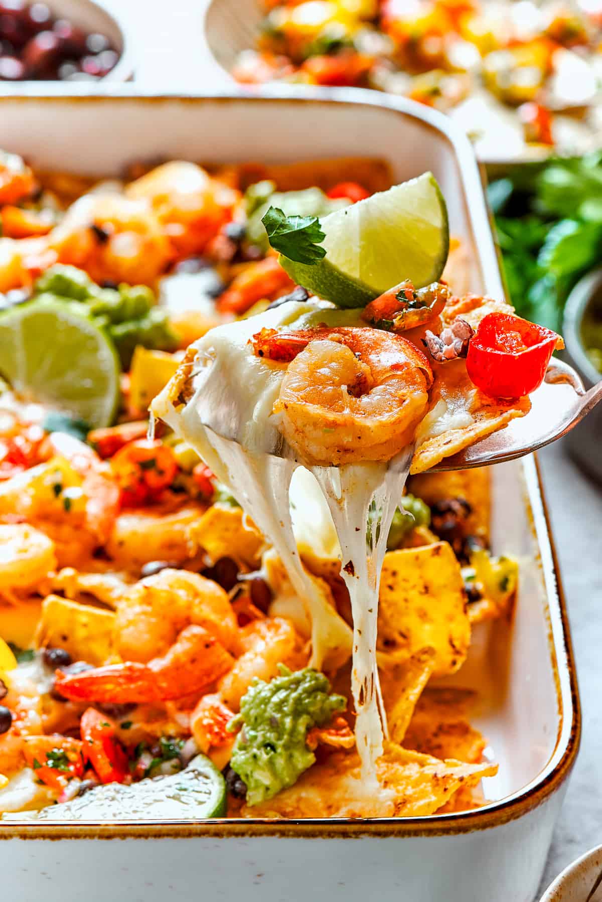 A spoon lifts out a cheesy portion of shrimp nachos.
