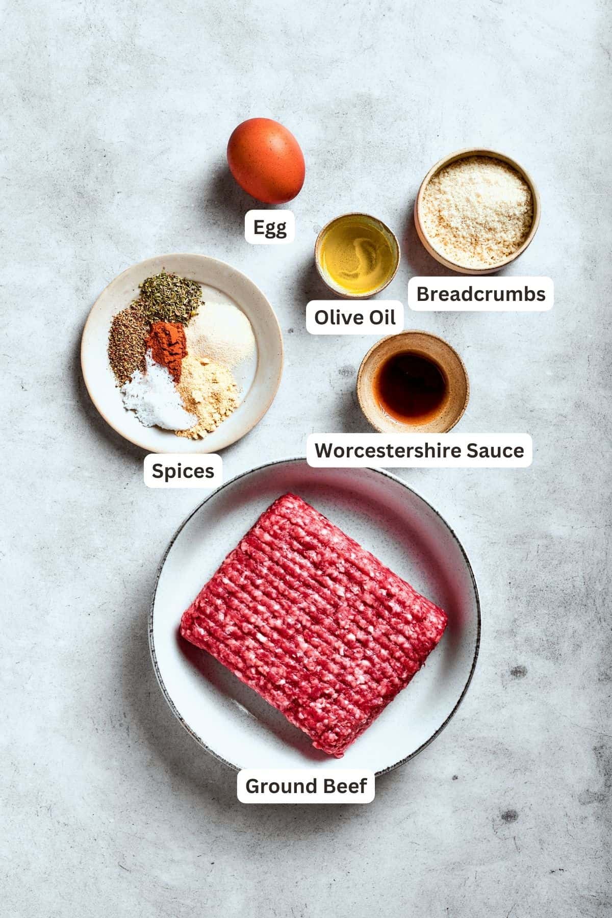 Ingredients for chopped steak are shown: ground beef, egg, seasonings, salt and pepper, olive oil, breadcrumbs.