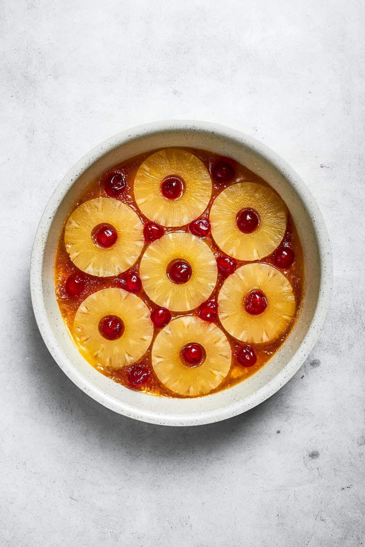 Pineapple rings are arranged neatly over the butter and brown sugar mixture, with maraschino cherries placed in their centers.