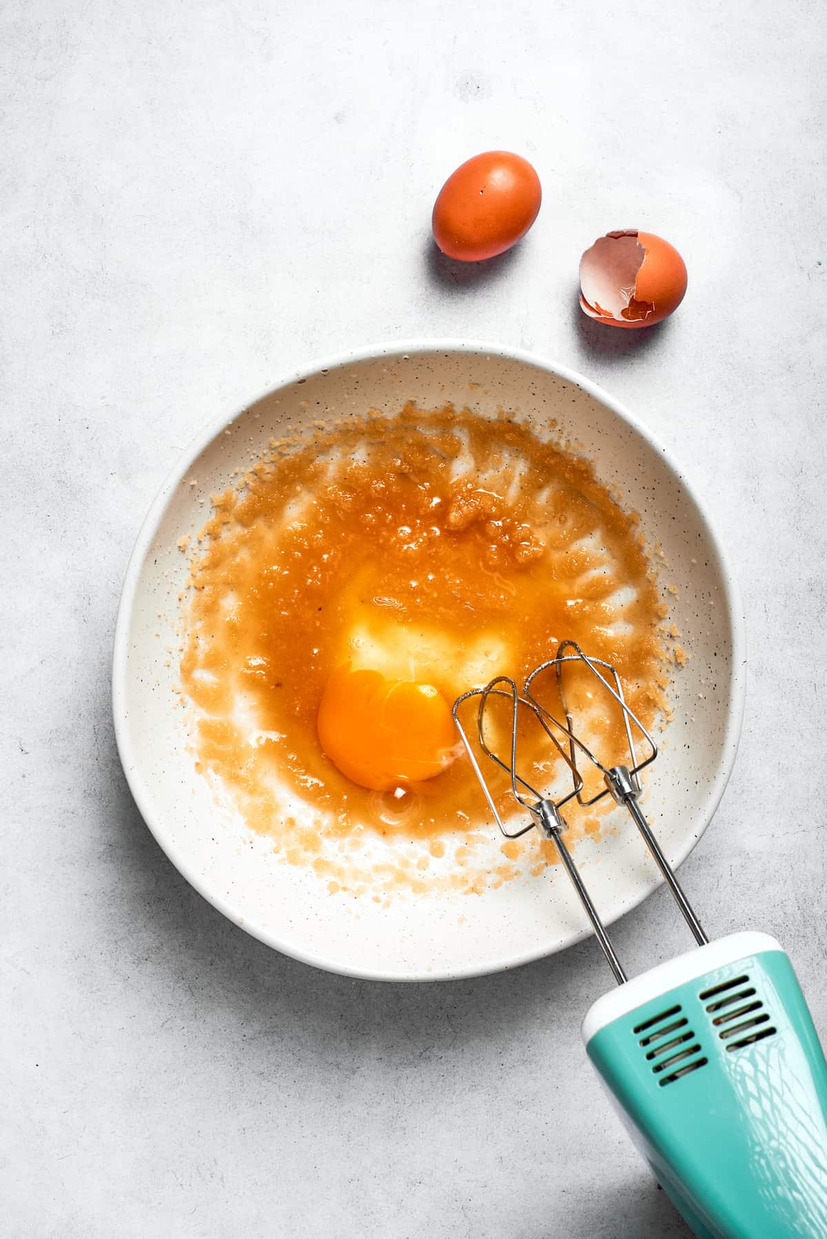 Eggs are being beaten into the oil and sugar mixture with a hand mixer until light and fluffy.
